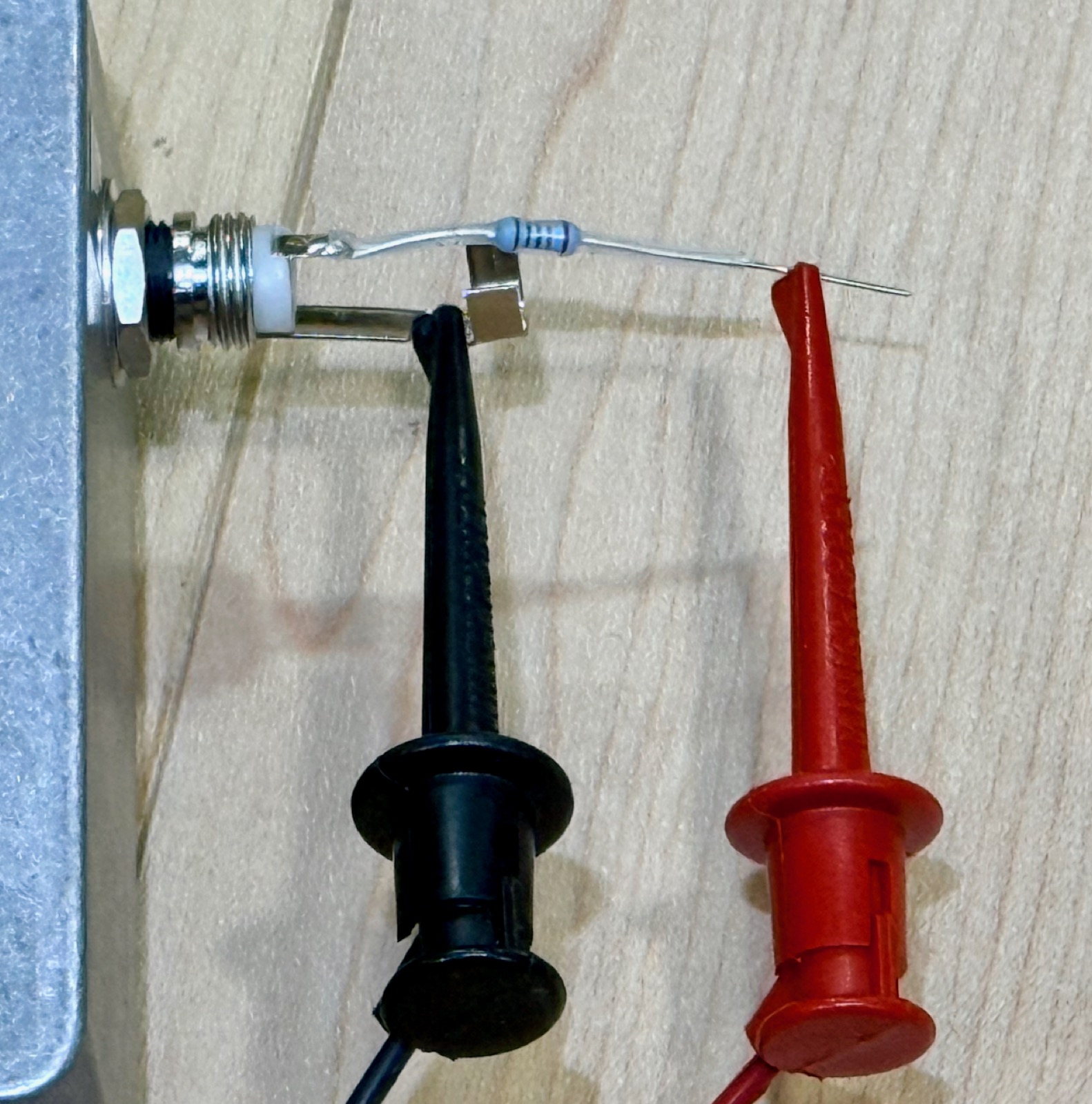 A bare ¼-inch plug seated in a jack, with a resistor soldered directly to its tip lug; the resistor's free lead is held by a red minigrabber clip while a black clip grounds the sleeve lug.